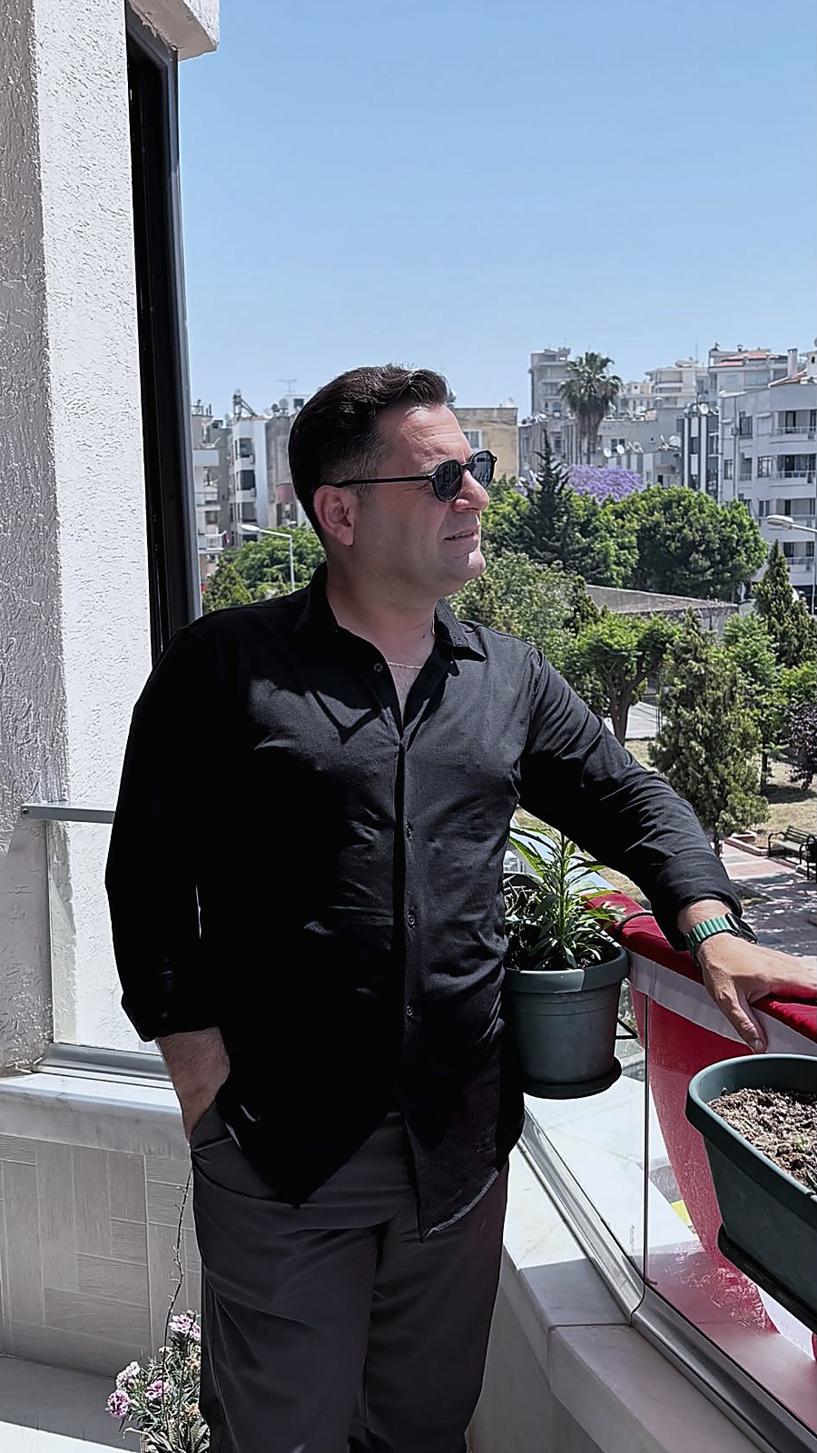 Feridun Özpolat, siyah gömlek ve güneş gözlüğüyle balkonda dururken